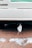 A disposable face mask is hanging from the rear of a vehicle parked on a red brick pavement. Melted patches of snow are scattered across the ground along with some cigarette butts.
