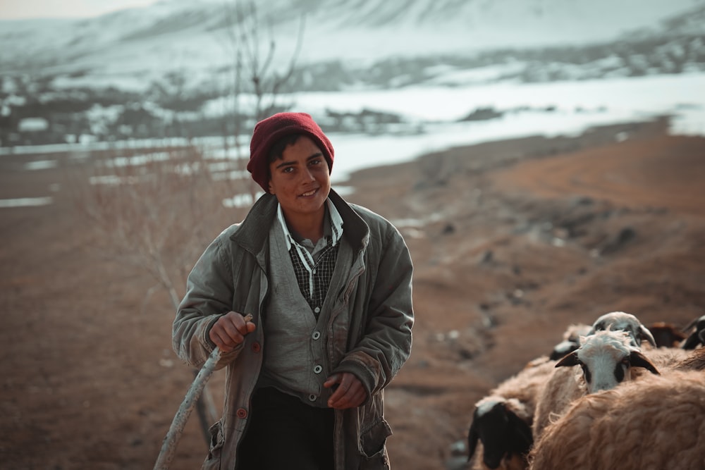 man in gray jacket and red knit cap standing beside brown horse during daytime