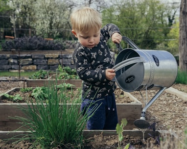 boy in black and white long sleeve shirt standing beside gray metal watering can during daytime