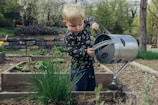 boy in black and white long sleeve shirt standing beside gray metal watering can during daytime