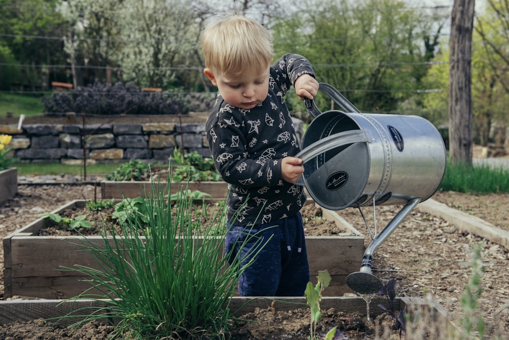 boy in black and white long sleeve shirt standing beside gray metal watering can during daytime