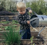 boy in black and white long sleeve shirt standing beside gray metal watering can during daytime