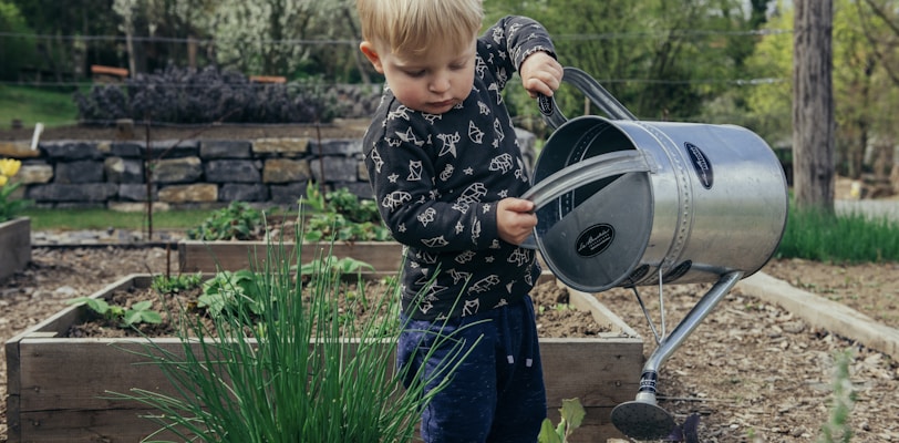 boy in black and white long sleeve shirt standing beside gray metal watering can during daytime