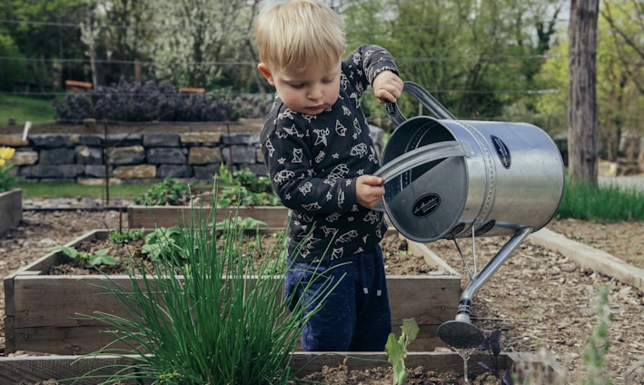 boy in black and white long sleeve shirt standing beside gray metal watering can during daytime