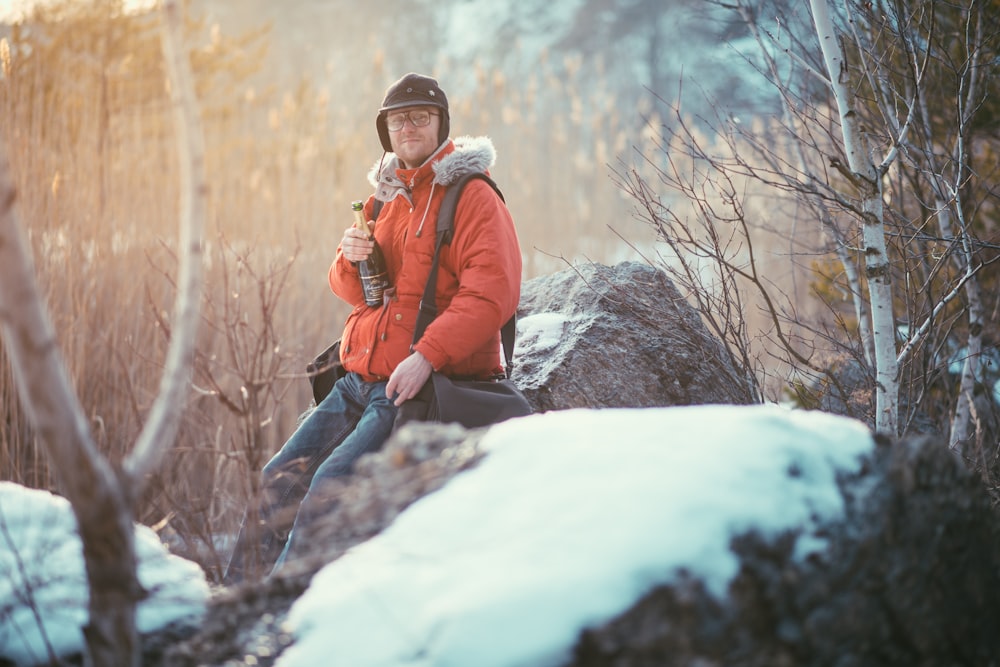 woman in red jacket and blue denim jeans sitting on snow covered ground during daytime