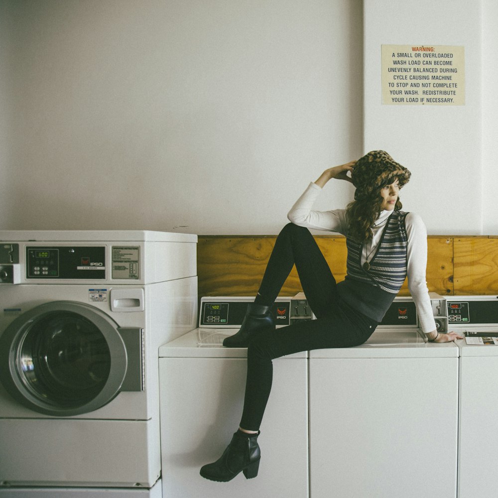 woman in black pants sitting on white front load washing machine