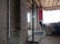 A partially constructed or renovated interior space featuring exposed brick walls and wooden ceilings. A white door is visible in the background next to a red painted wall. A plastic sheet covers furniture on the right side, and there are construction materials scattered across the floor.