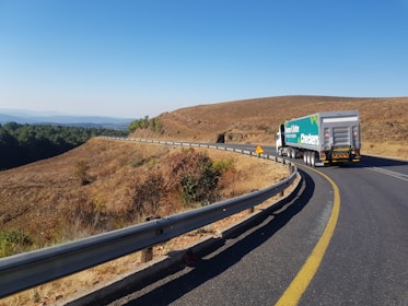 Truck loaded with cargo on highway winding through green hills in daylight.