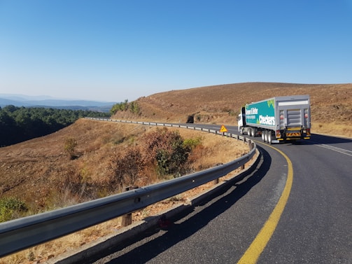 A sturdy cargo truck driving along a winding highway surrounded by green hills.