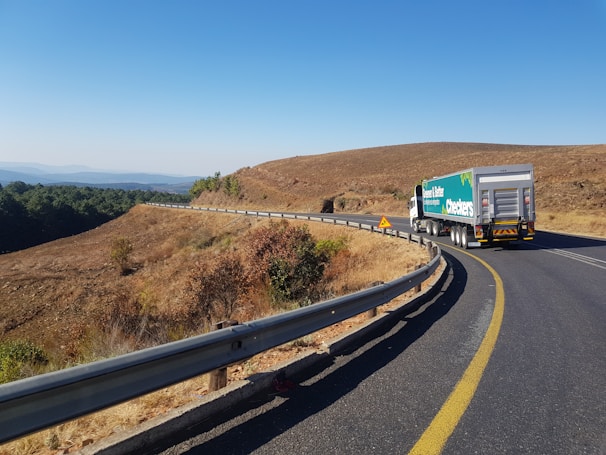 Close-up of a loaded cargo truck on a highway surrounded by green hills.