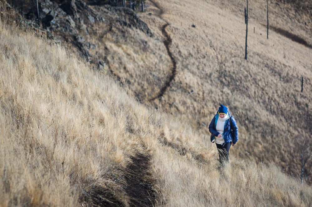 person in blue jacket walking on brown grass field during daytime