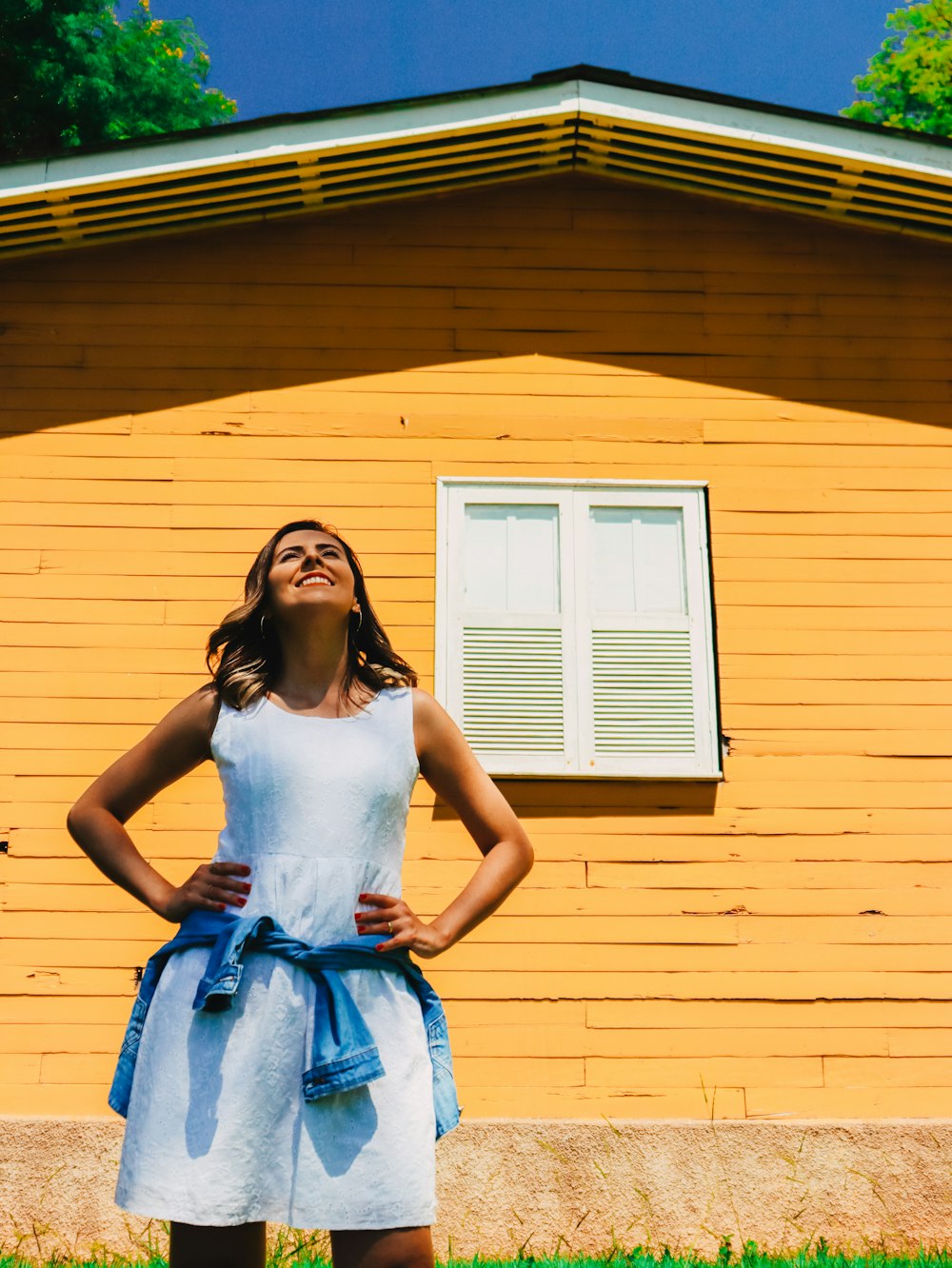 femme en débardeur blanc et jupe bleue debout devant la maison jaune