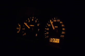 A dimly lit car dashboard with illuminated speedometer and tachometer gauges. The speedometer reads approximately 60 km/h, and the tachometer shows an engine RPM of around 3,000. The digital odometer displays the current reading of 239,836 kilometers.
