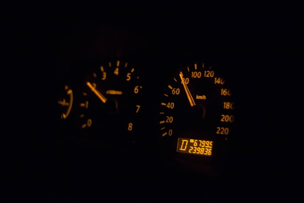 A dimly lit car dashboard with illuminated speedometer and tachometer gauges. The speedometer reads approximately 60 km/h, and the tachometer shows an engine RPM of around 3,000. The digital odometer displays the current reading of 239,836 kilometers.