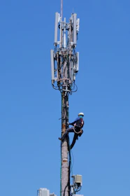 Technician working on a telecommunications tower with safety gear.