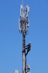 A rugged telecommunications technician confidently wearing turtel armor safety gear on a high tower at sunset.