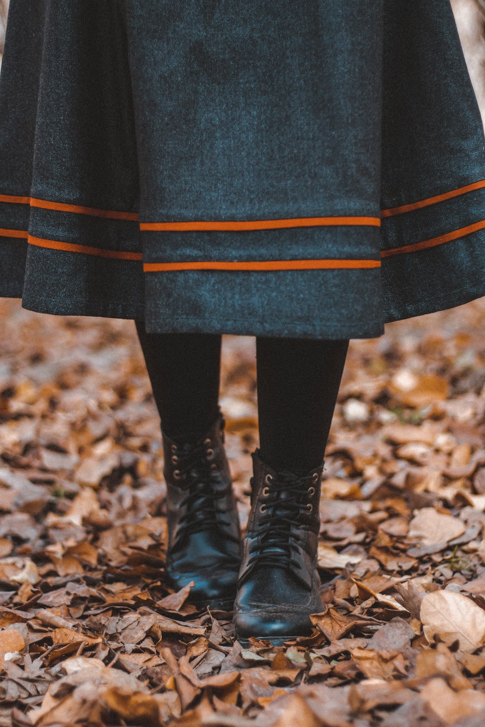 person in black leather boots standing on dried leaves