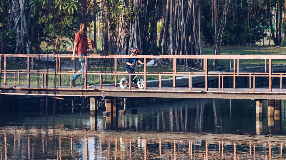 man in red jacket and black pants sitting on brown wooden dock during daytime