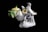Porcelain figurine depicting two white birds with intricate details, perched among colorful flowers, next to a green ceramic teapot with a yellow lid. The composition is set against a dark background, showcasing the smooth and glossy finish of the ceramics.