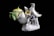 Porcelain figurine depicting two white birds with intricate details, perched among colorful flowers, next to a green ceramic teapot with a yellow lid. The composition is set against a dark background, showcasing the smooth and glossy finish of the ceramics.