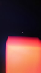 A dark background with a prominent glowing rectangular form in shades of red and orange, and a faint squiggly line of light above it.