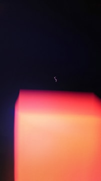 A dark background with a prominent glowing rectangular form in shades of red and orange, and a faint squiggly line of light above it.