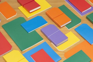 A colorful assortment of school notebooks and journals neatly stacked on a wooden desk.