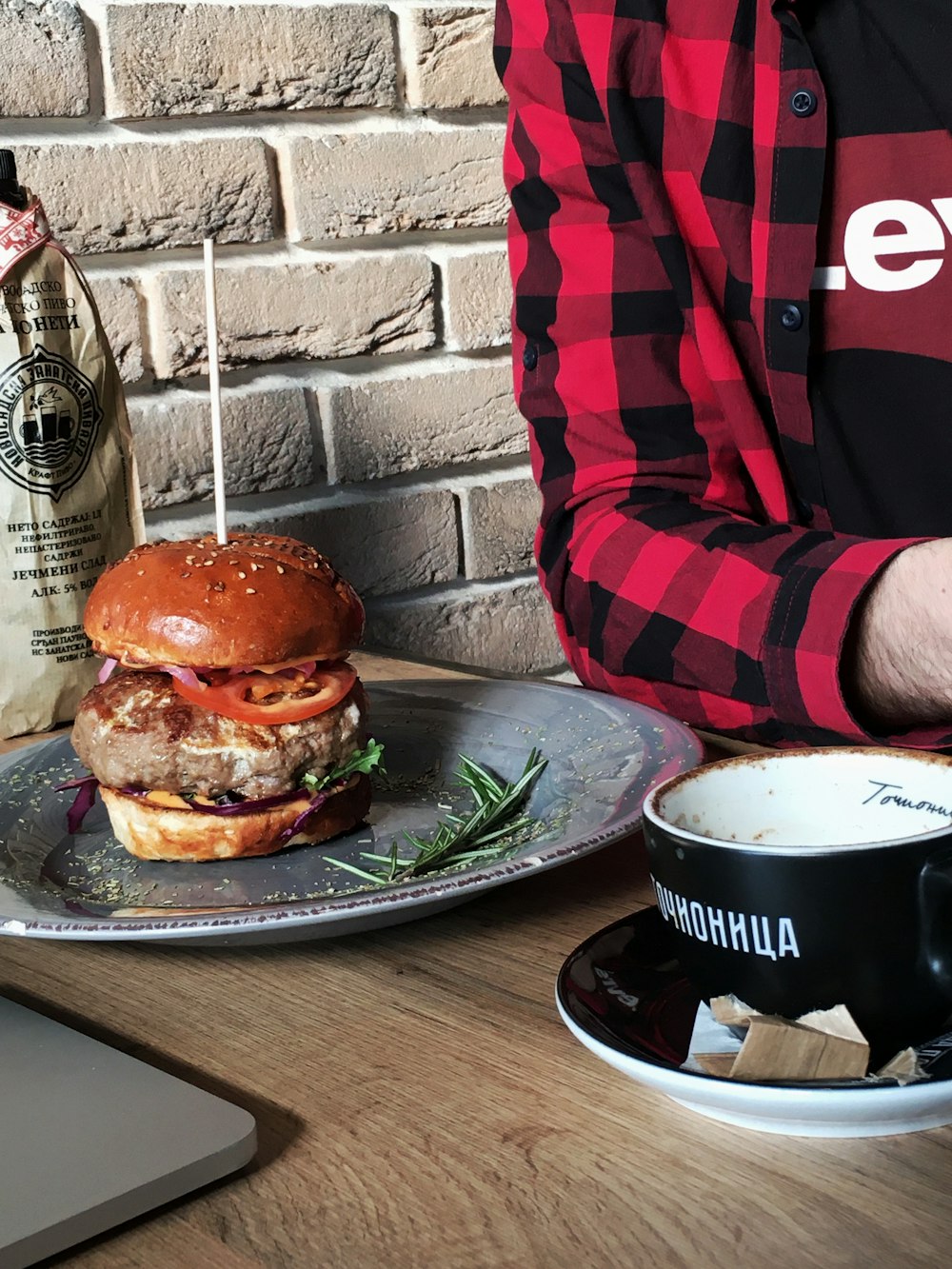 Un hombre sosteniendo un plato con una hamburguesa y una taza de café