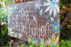 Rustic wooden garden sign with hand-painted floral designs nestled among blooming garden beds