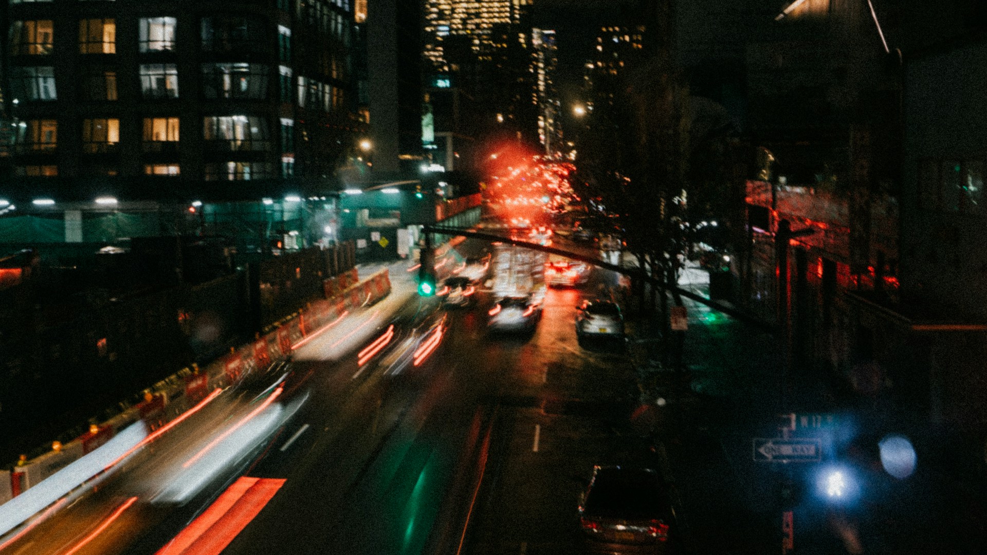A bustling city street at night, alive with glowing lights and the blur of passing cars.