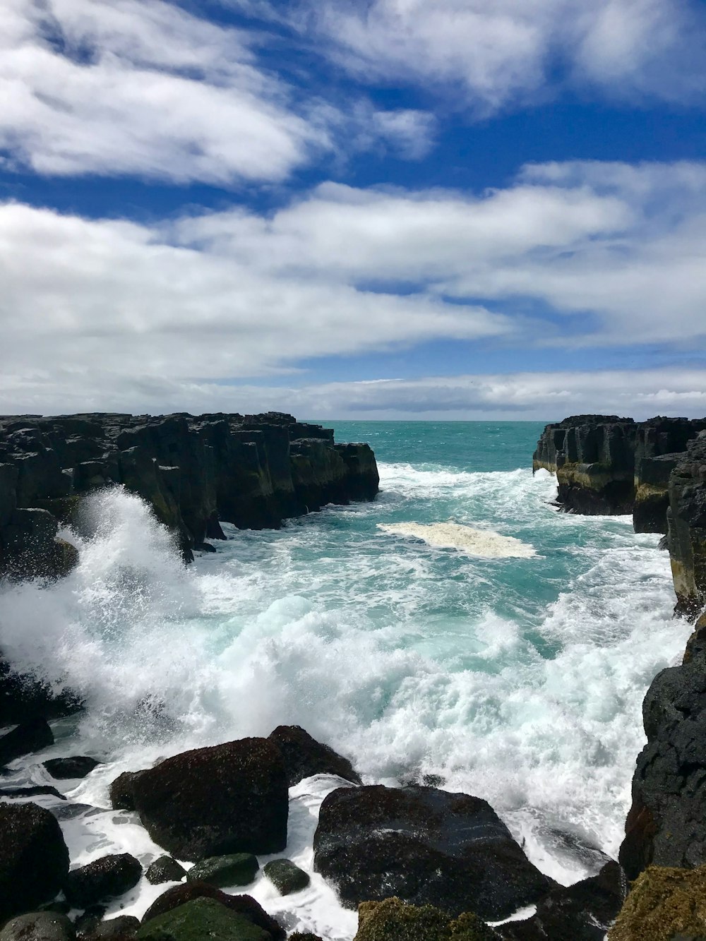 ocean waves crashing on rocky shore under cloudy sky during daytime