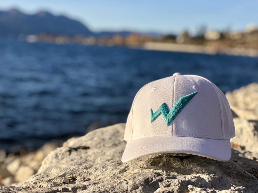 white and teal nike cap on gray rock near body of water during daytime