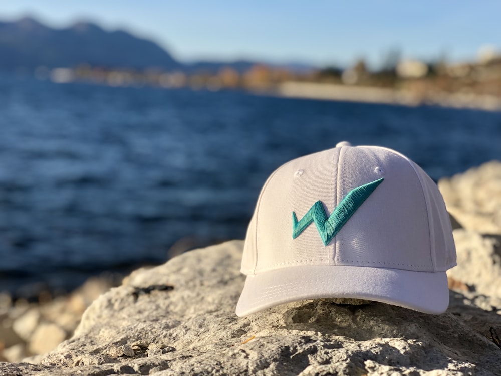 casquette Nike blanche et turquoise sur roche grise près du plan d’eau pendant la journée