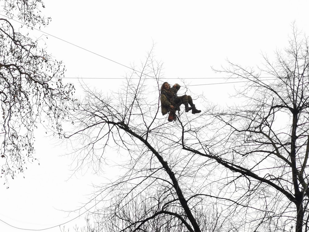 man in brown jacket and black pants sitting on brown tree branch during daytime