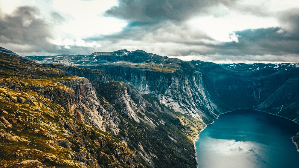 brown and green mountain beside body of water under cloudy sky during daytime