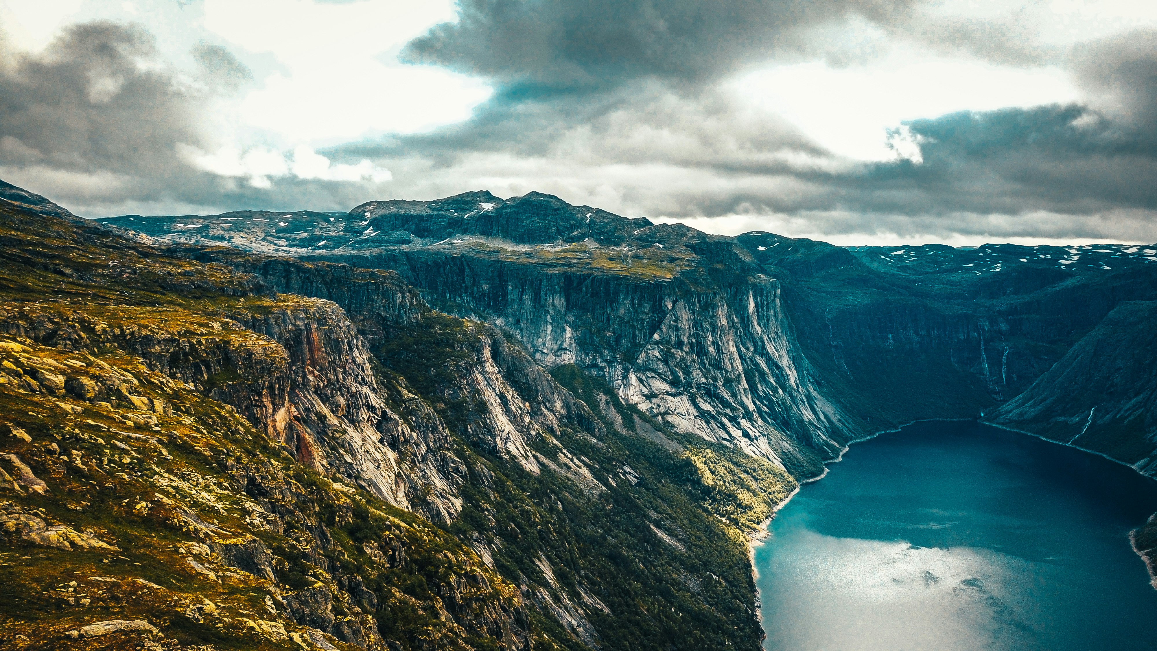 brown and green mountain beside body of water under cloudy sky during daytime