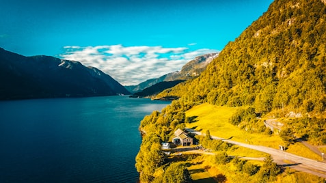 brown house on green grass field near body of water under blue sky during daytime