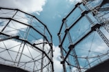 Two large metal structures with complex frameworks rise against a partly cloudy sky, creating an industrial and geometric appearance with their lattice-like design.