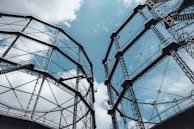 Two large metal structures with complex frameworks rise against a partly cloudy sky, creating an industrial and geometric appearance with their lattice-like design.