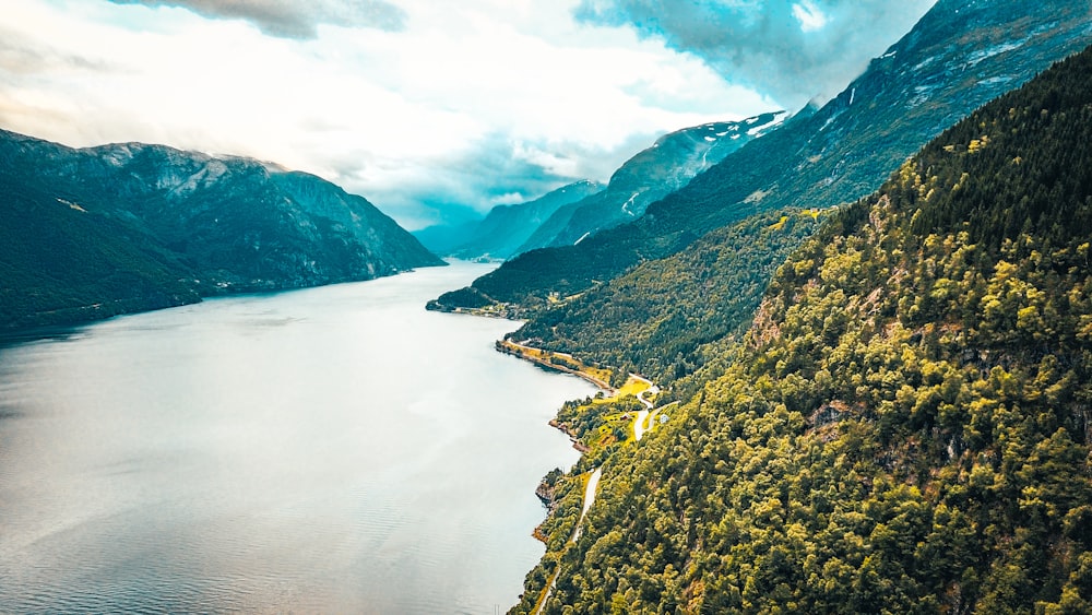 green and brown mountains beside river under white clouds and blue sky during daytime