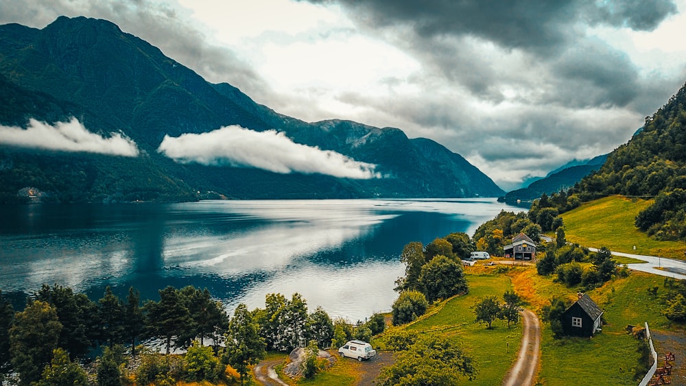 green trees near lake and mountains under white clouds during daytime