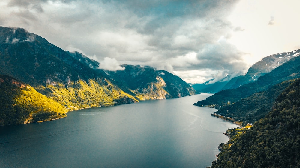 green and yellow mountains beside lake under cloudy sky during daytime