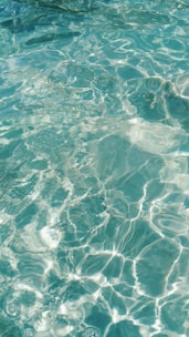Clear, shimmering water with sunlight creating intricate patterns on the surface, providing a sense of freshness and tranquility.