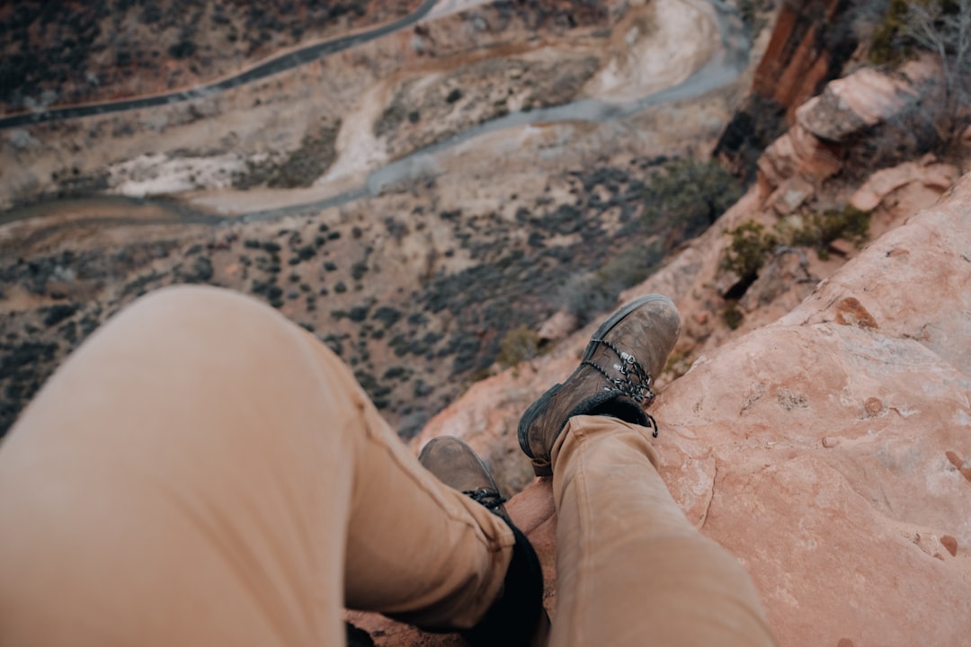 person in brown pants and black hiking shoes sitting on brown rock during daytime