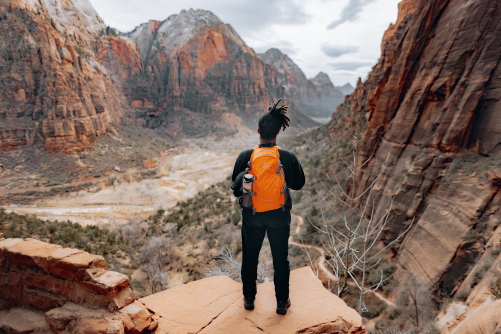 woman in black and orange jacket standing on brown rock formation during daytime