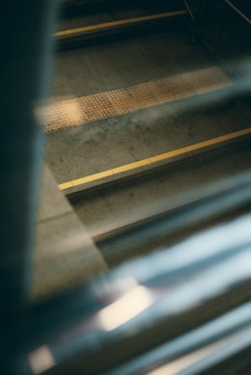A series of stairs with a textured, yellow tactile strip along the edge, seen through a reflective surface creating a blurred effect at the foreground.