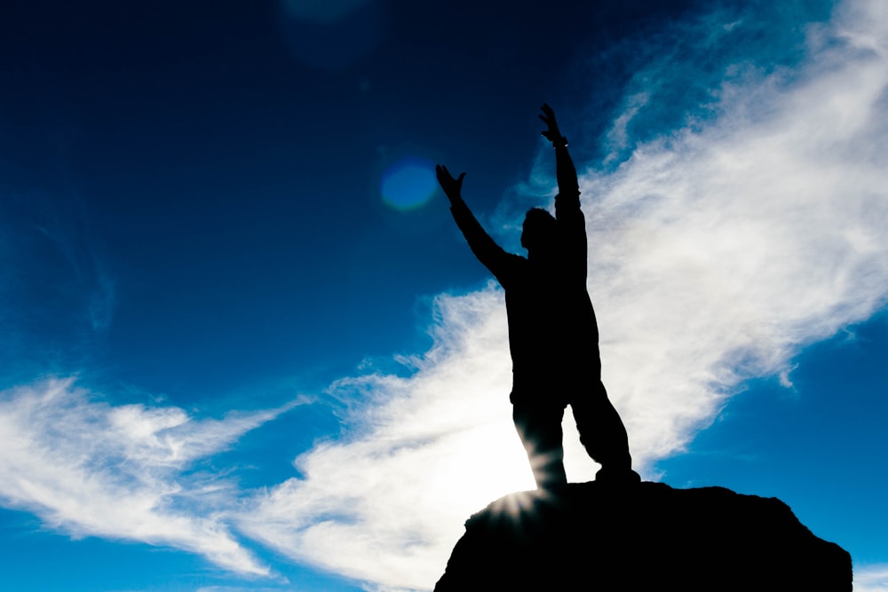 silhouette of man raising his hands under blue sky during daytime