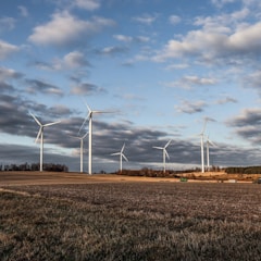 white wind turbines on brown grass field under white clouds and blue sky during daytime