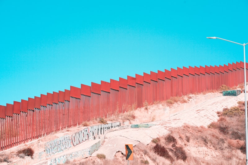 Red metal border fence stretching across sandy terrain under a blue sky