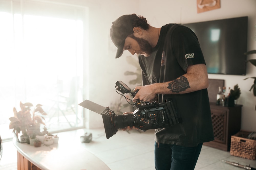 man in black crew neck t-shirt and blue denim jeans holding black dslr camera